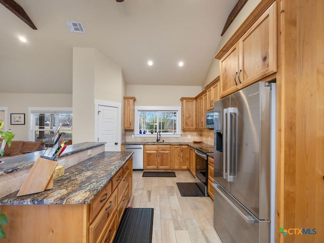 kitchen featuring lofted ceiling, a sink, visible vents, appliances with stainless steel finishes, and dark stone countertops