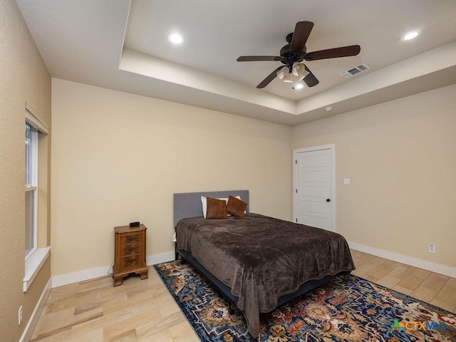 bedroom with baseboards, a raised ceiling, visible vents, and light wood-style floors