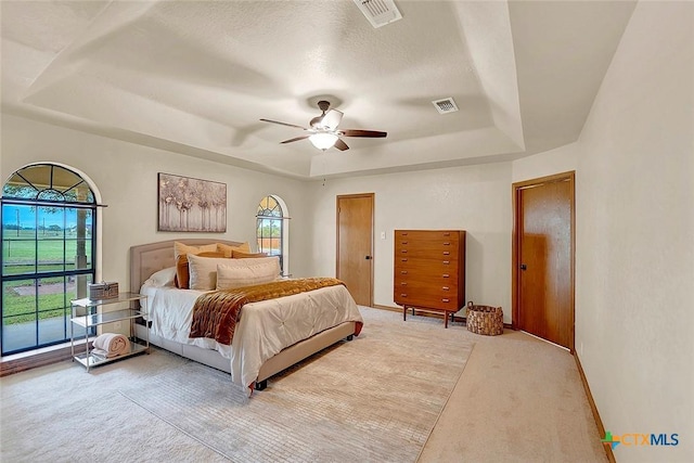 bedroom with a raised ceiling, light colored carpet, ceiling fan, and baseboards