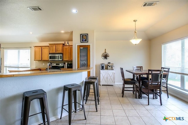 2406 Peace Pipe Cir, Copperas Cove, TX 76522 - kitchen with stainless steel microwave, a breakfast bar, brown cabinetry, range, and plenty of natural light