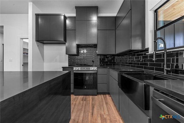 kitchen with wood-type flooring, dark stone countertops, stainless steel appliances, backsplash, and gray cabinets