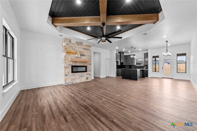 unfurnished living room featuring beam ceiling, dark wood-type flooring, a fireplace, and ceiling fan with notable chandelier