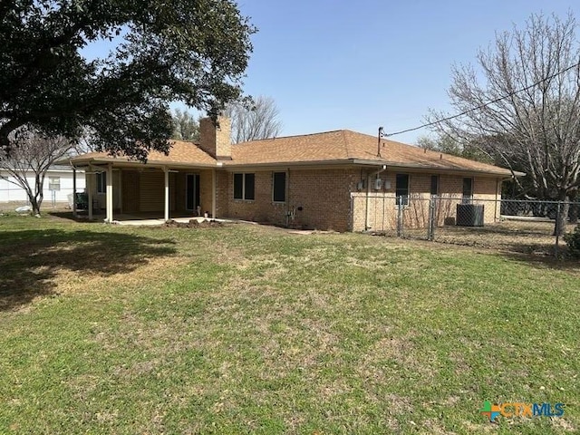 back of property featuring central AC unit, brick siding, fence, a yard, and a chimney