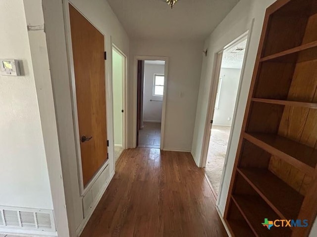 hallway with visible vents, baseboards, and wood finished floors