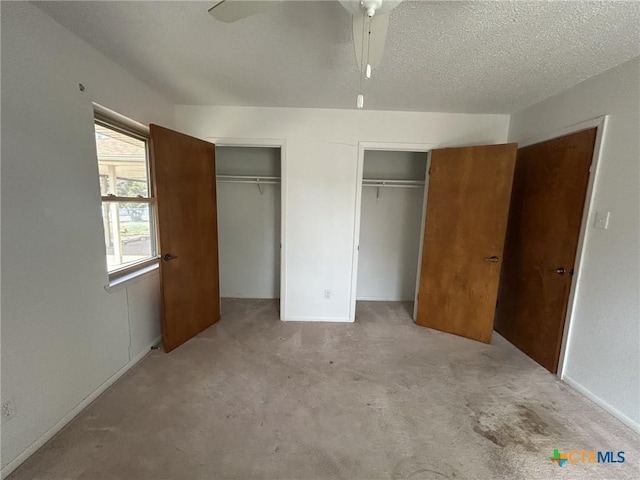 unfurnished bedroom with a textured ceiling, carpet floors, two closets, and a ceiling fan