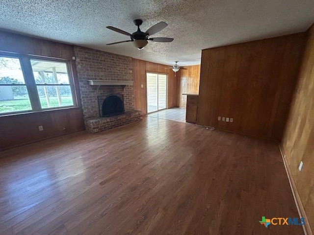 unfurnished living room with a fireplace, ceiling fan, wood walls, a textured ceiling, and wood finished floors