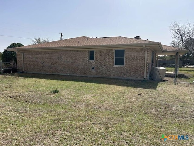 rear view of house with a shingled roof, brick siding, a yard, and fence