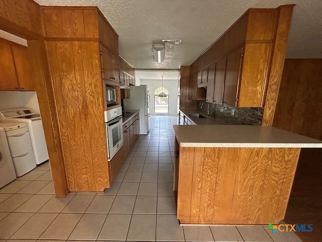 kitchen with brown cabinetry, washer and dryer, stainless steel oven, a sink, and light tile patterned flooring