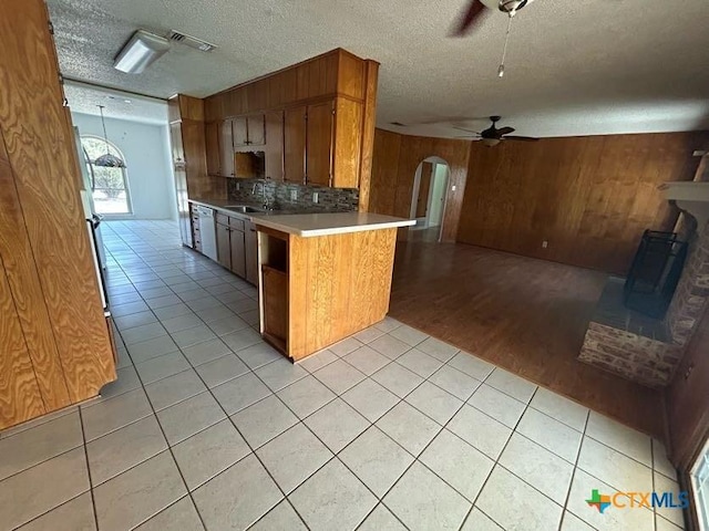 kitchen featuring arched walkways, ceiling fan, wood walls, open floor plan, and brown cabinets