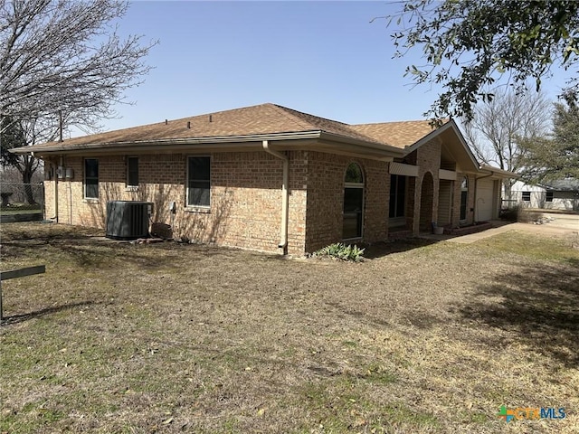 view of side of home featuring a garage, cooling unit, brick siding, and roof with shingles