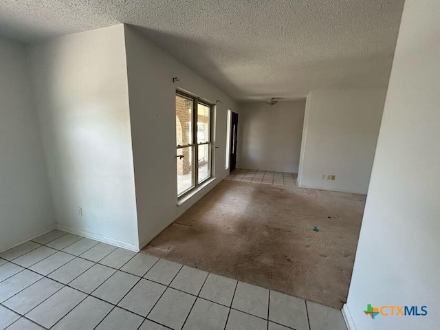 spare room with light tile patterned floors, a textured ceiling, and light colored carpet