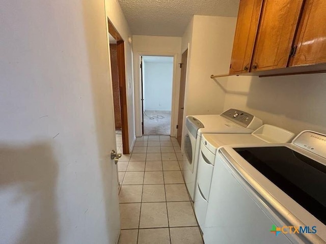 laundry area featuring cabinet space, light tile patterned floors, washer and clothes dryer, and a textured ceiling