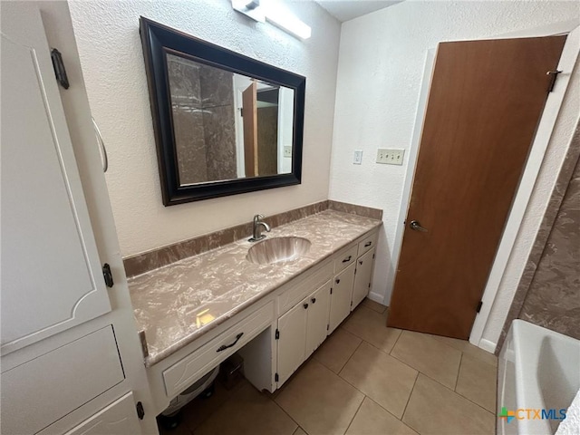 bathroom with a textured wall, tile patterned flooring, a bathtub, and vanity