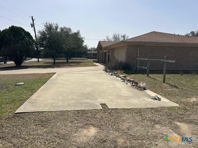 exterior space featuring a garage, driveway, brick siding, and roof with shingles