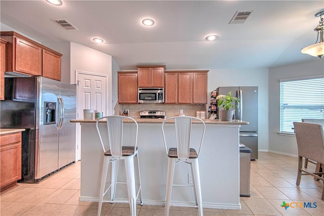 kitchen featuring appliances with stainless steel finishes, brown cabinetry, visible vents, and a kitchen bar