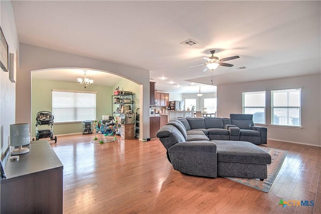 living room featuring arched walkways, ceiling fan with notable chandelier, visible vents, baseboards, and light wood-type flooring