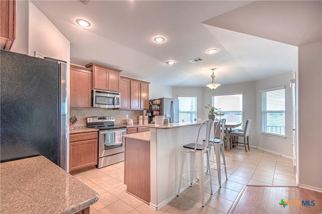 kitchen featuring a center island, decorative light fixtures, tasteful backsplash, visible vents, and appliances with stainless steel finishes