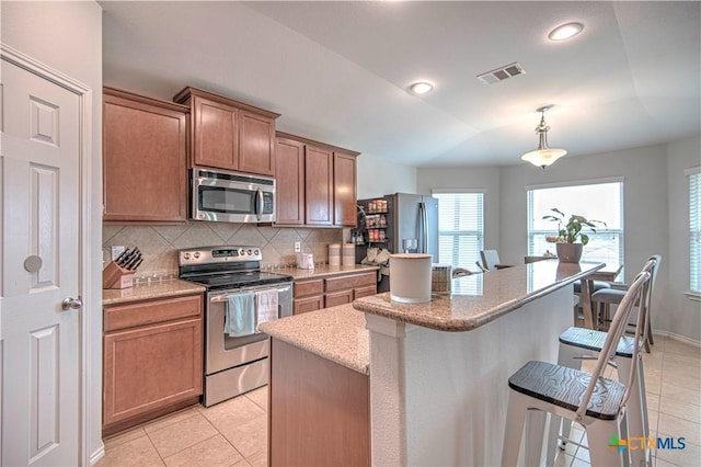 kitchen with brown cabinetry, a kitchen island, appliances with stainless steel finishes, a kitchen breakfast bar, and pendant lighting