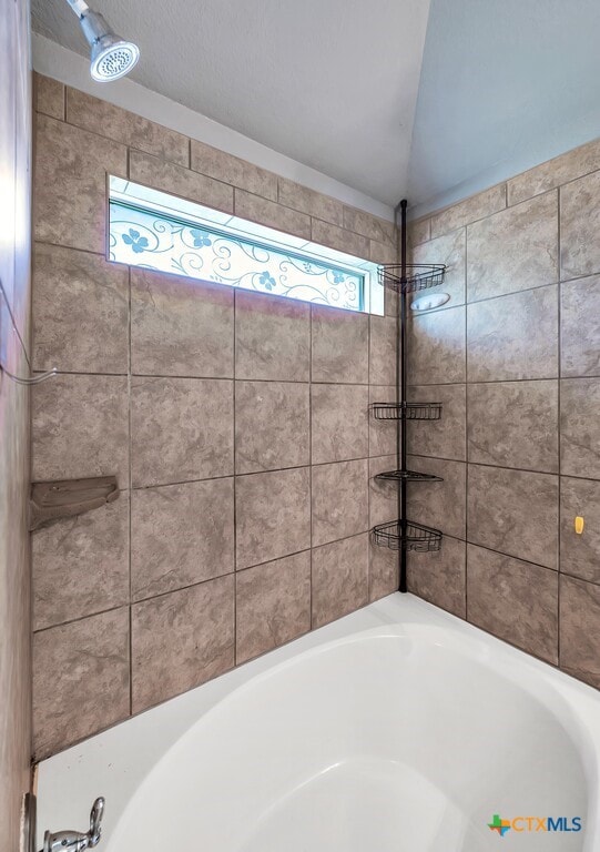 bathroom featuring tiled shower / bath combo, vaulted ceiling, and plenty of natural light