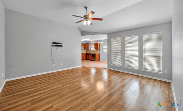 unfurnished living room with ceiling fan with notable chandelier, light hardwood / wood-style flooring, and vaulted ceiling