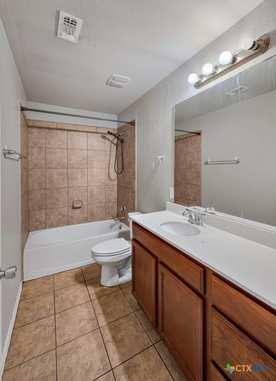 full bathroom with tile patterned floors, vanity, a textured ceiling, toilet, and tiled shower / bath