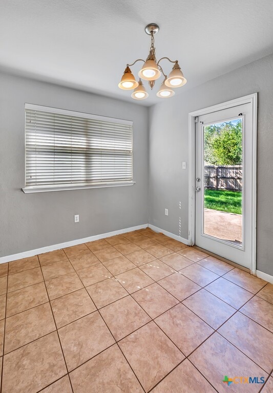 tiled spare room featuring an inviting chandelier