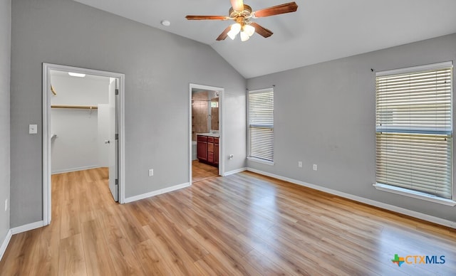 unfurnished bedroom with a walk in closet, vaulted ceiling, multiple windows, and light hardwood / wood-style floors