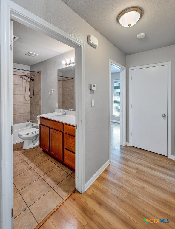 full bathroom with hardwood / wood-style floors, a textured ceiling, vanity, and tiled shower / bath combo