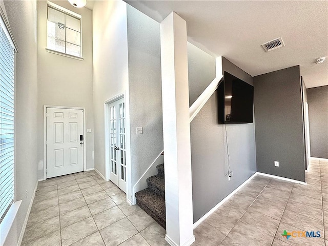 foyer featuring a high ceiling, plenty of natural light, light tile patterned floors, and french doors