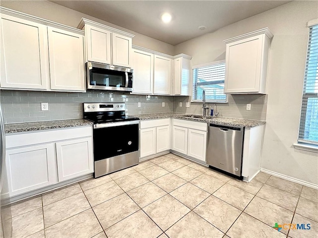 kitchen with light stone countertops, white cabinets, appliances with stainless steel finishes, and sink