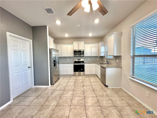 kitchen featuring ceiling fan, stainless steel appliances, white cabinets, light stone counters, and sink