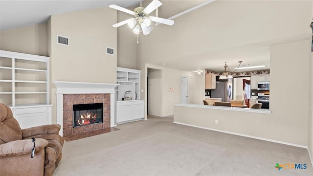 living area with light carpet, vaulted ceiling, a tile fireplace, and visible vents