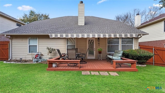 rear view of house featuring a shingled roof, a lawn, a chimney, fence, and a wooden deck