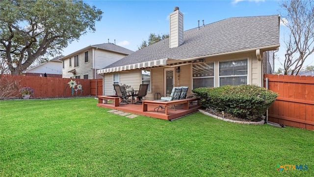 back of house with a fenced backyard, roof with shingles, a lawn, a wooden deck, and a chimney