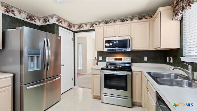 kitchen with appliances with stainless steel finishes, cream cabinetry, light countertops, and a sink