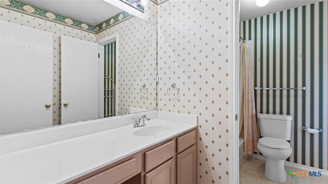 bathroom featuring tile patterned flooring, toilet, vanity, baseboards, and wallpapered walls