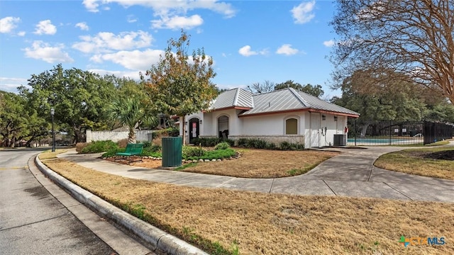 view of front of property with metal roof, stucco siding, fence, and central air condition unit