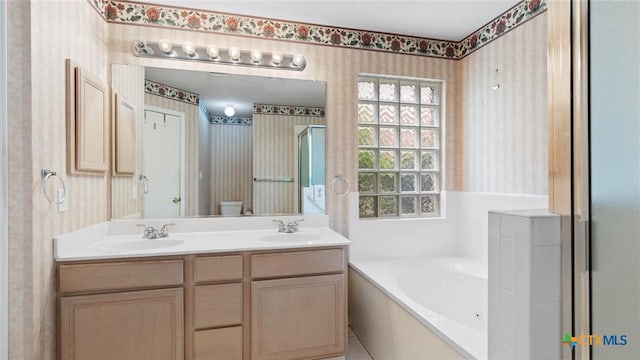 bathroom with a bath, wallpapered walls, double vanity, and a sink