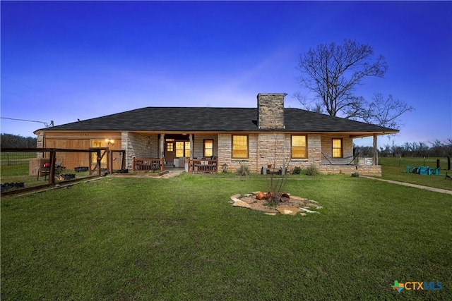 back of house at dusk with stone siding, a lawn, and a chimney