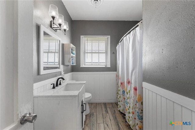 bathroom with a wainscoted wall, toilet, a healthy amount of sunlight, and wood finished floors