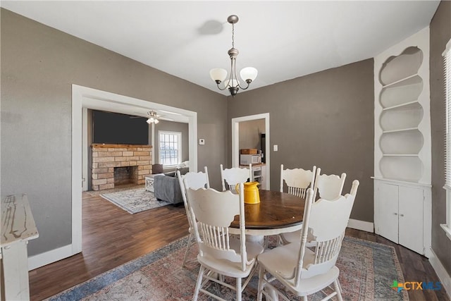 dining area featuring baseboards, wood finished floors, a fireplace, and ceiling fan with notable chandelier