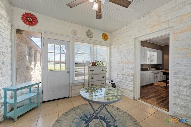 entryway featuring light tile patterned floors, brick wall, and a ceiling fan