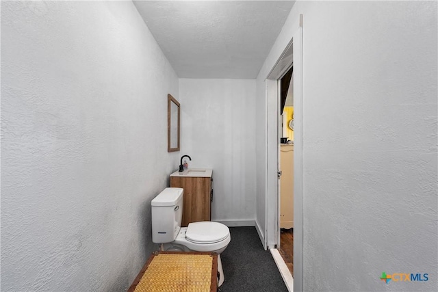 bathroom featuring baseboards, toilet, a textured wall, and a sink