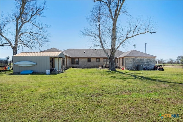 back of house featuring a yard, a trampoline, and an outdoor structure