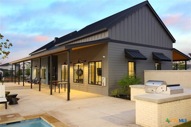192 Lavender Ln, Elgin, TX 78621 - back of house at dusk featuring an outdoor kitchen, board and batten siding, a standing seam roof, and a patio area