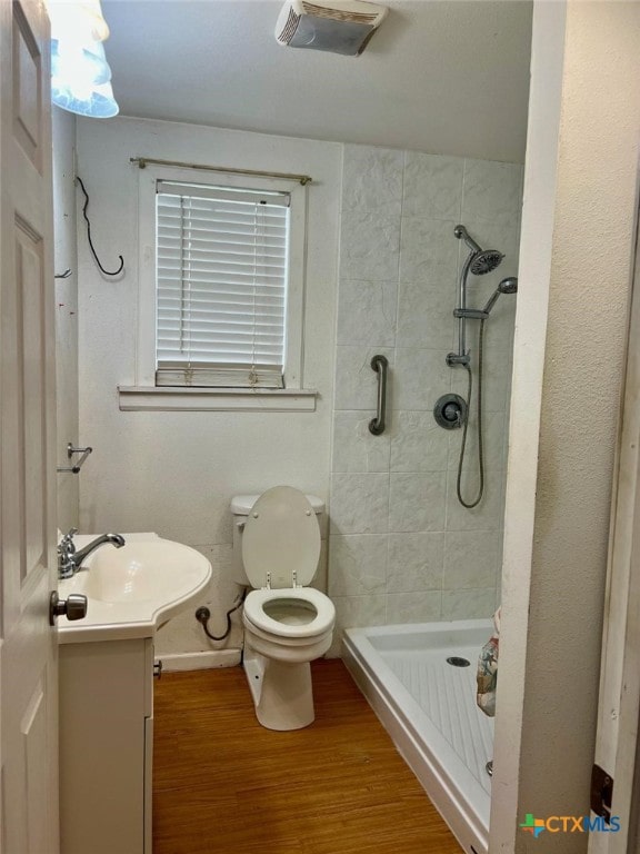 bathroom featuring vanity, toilet, hardwood / wood-style floors, and a tile shower