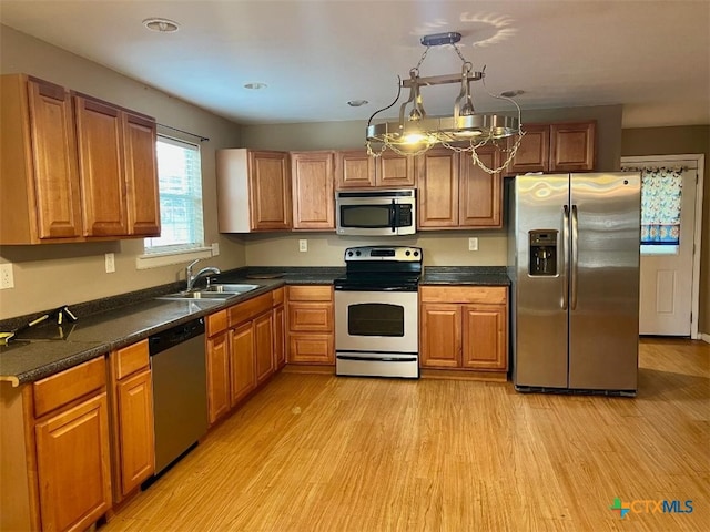 kitchen with appliances with stainless steel finishes, sink, light hardwood / wood-style floors, and hanging light fixtures