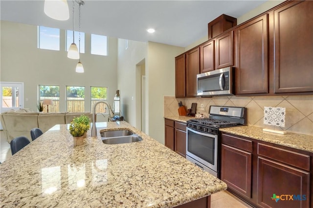 kitchen with decorative light fixtures, stainless steel appliances, sink, backsplash, and light stone counters