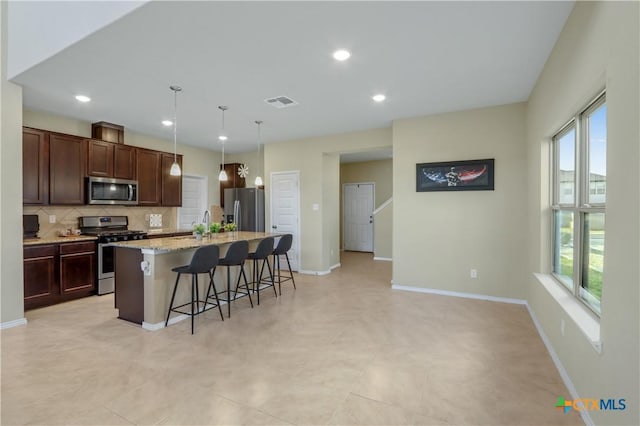 kitchen with stainless steel appliances, tasteful backsplash, a kitchen island with sink, a kitchen breakfast bar, and dark brown cabinets