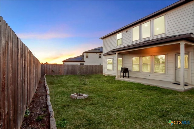 back house at dusk with a patio and a yard